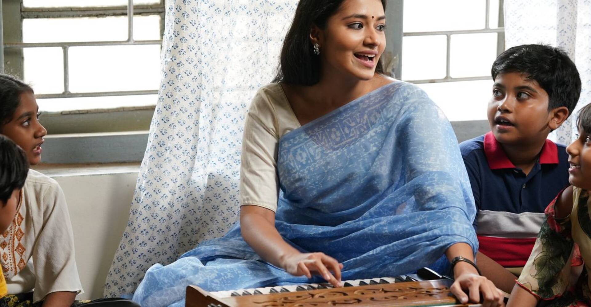 A young woman teaching a group of children at a harmonium